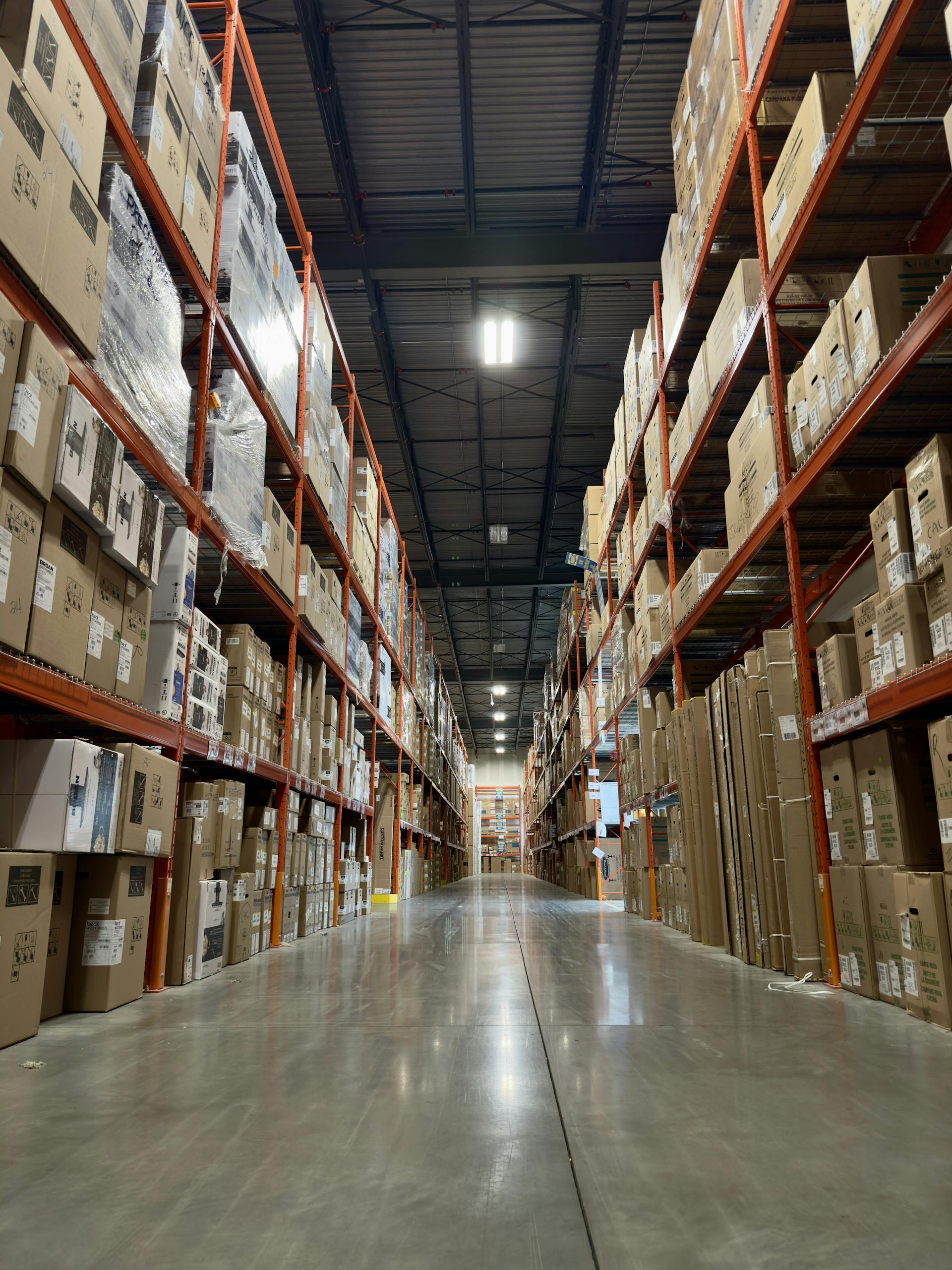 Long aisle in a busy warehouse stacked with boxes and products on shelves.